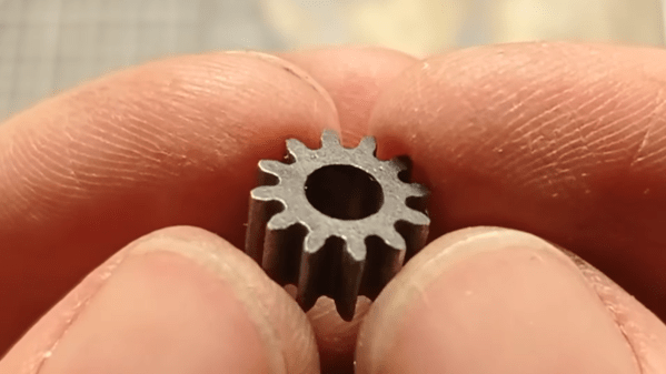 A fine steel gear is shown held between a man's fingertips.